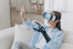 European handicapped girl in vr glasses on sofa at home. Healing technology, robotic limb.