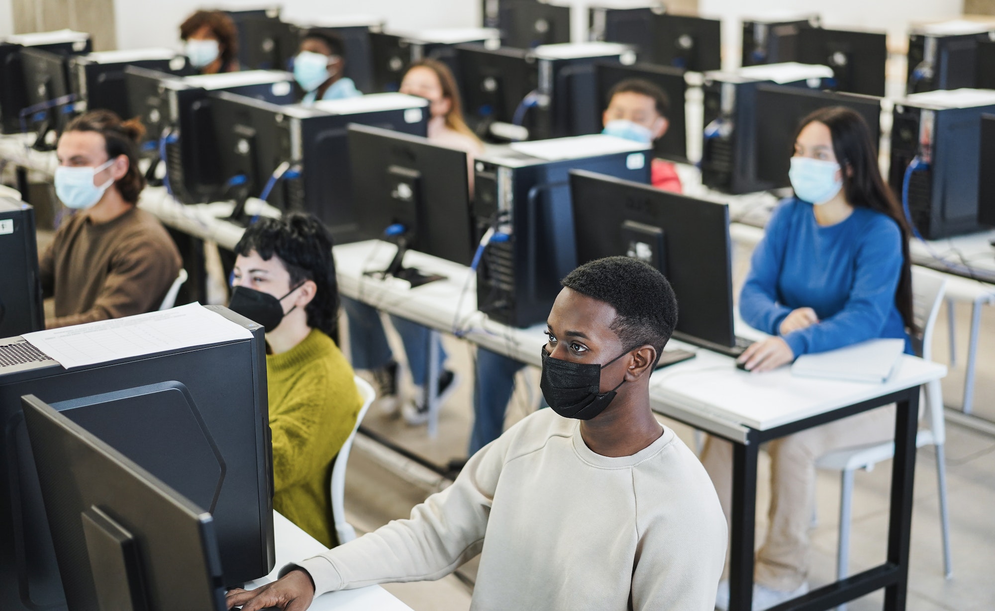Young multiracial students using computers wearing protective mask inside technology class at school